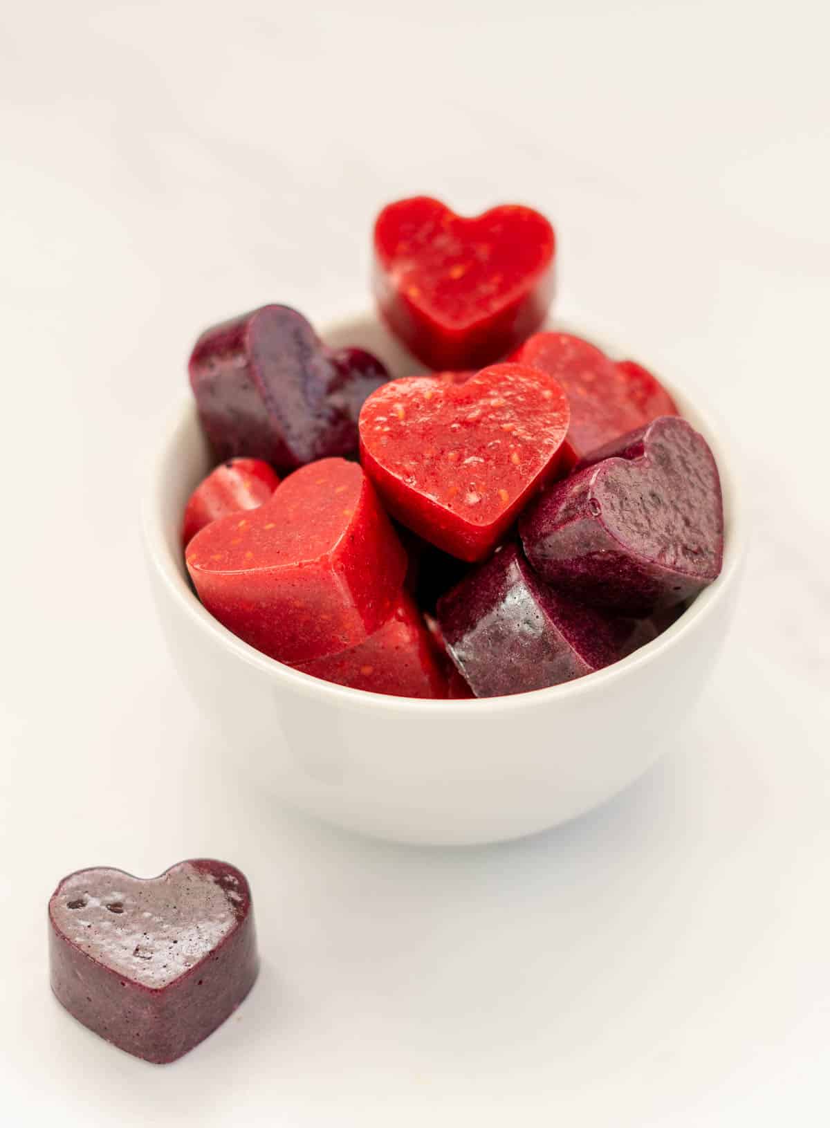 a small white bowl filled with heart shaped red and purple berry gummies 