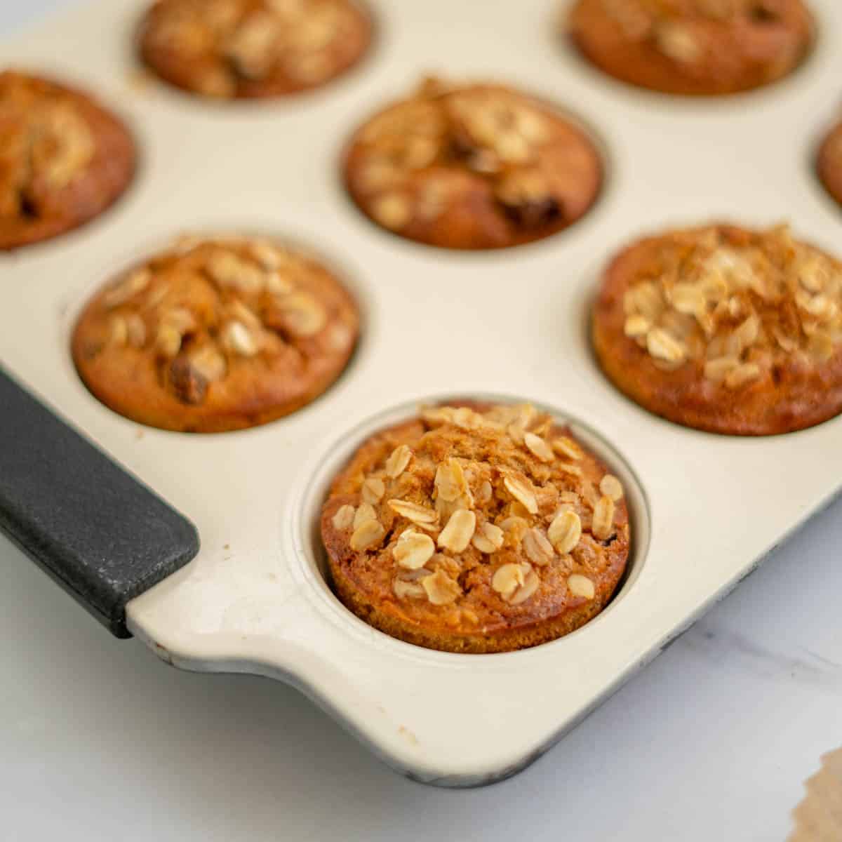 Baked muffins topped with oatmeal in a cream muffin tray