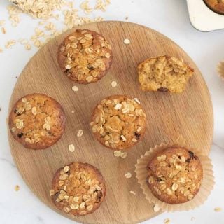 top down shot of oatmeal muffins on a round wooden tray with a scoop of rolled oats