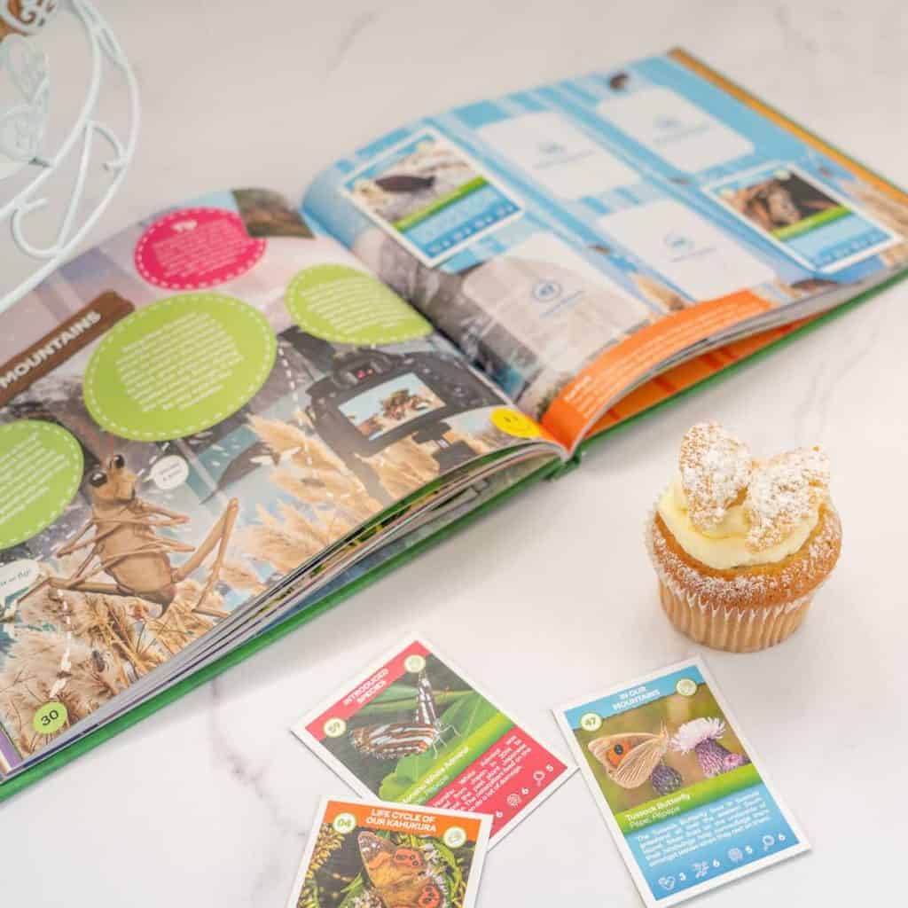 A insect book and cards with a butterfly cupcake in front of them