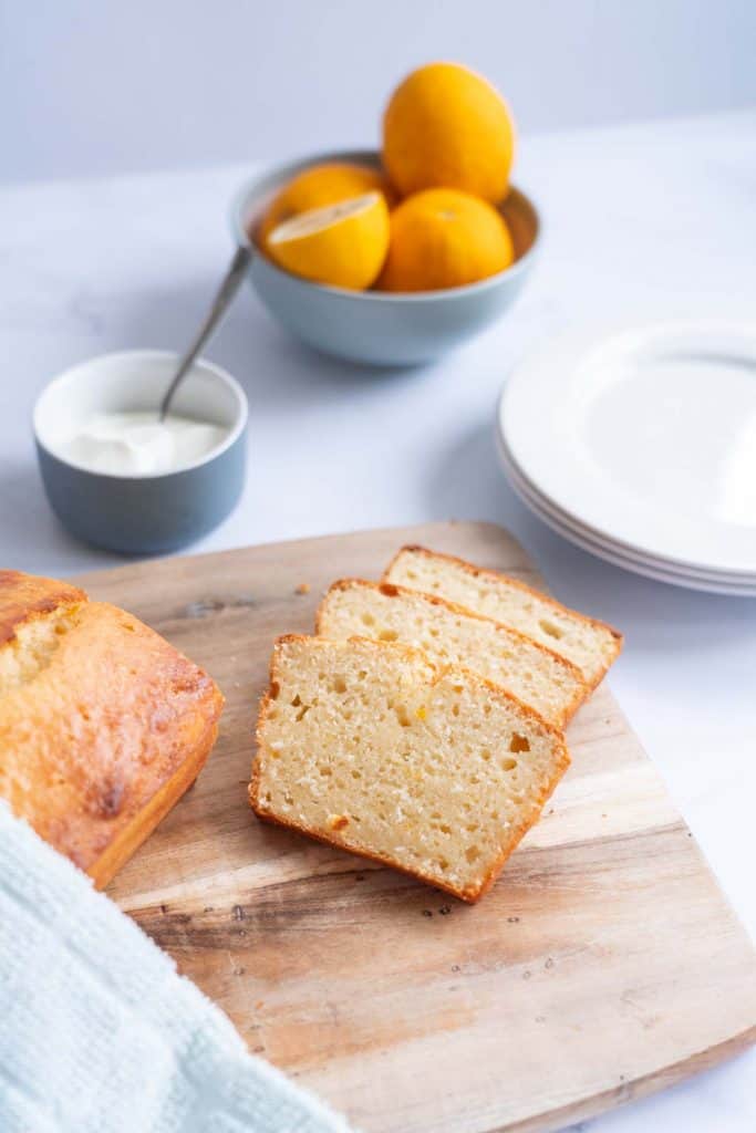 Lemon loaf sliced on chopping board with greek yogurt in background blurred.