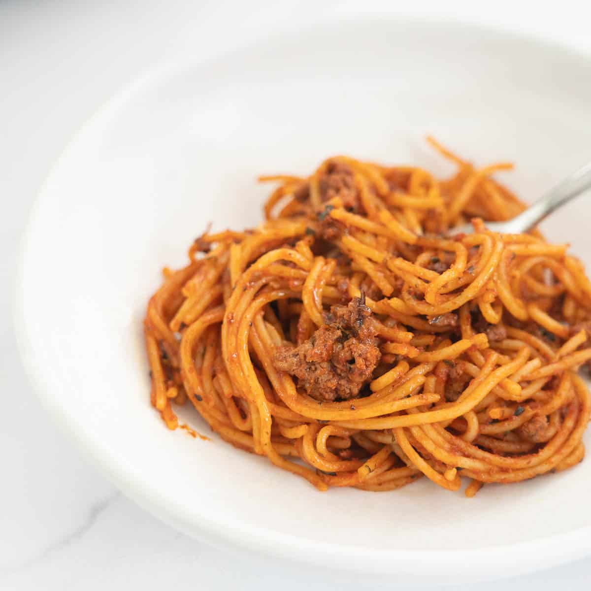 spaghetti bolognese in a white bowl with fork