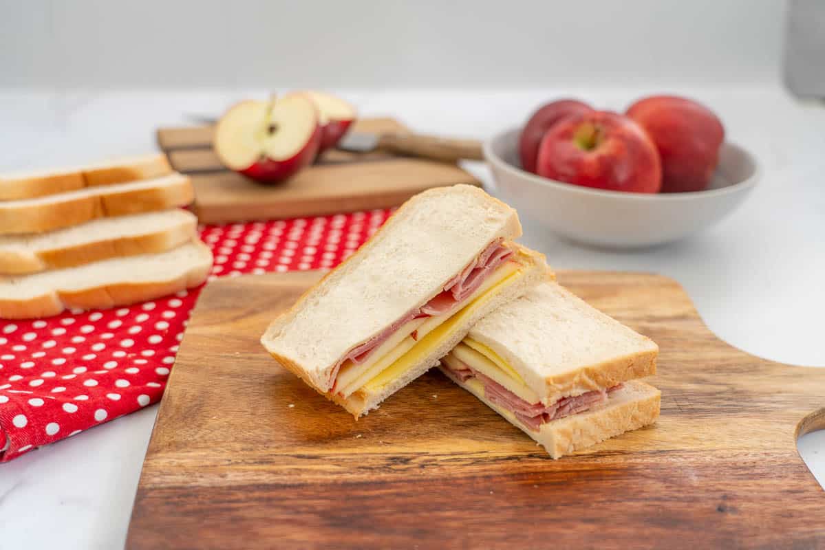 sandwich filled with apple, ham and cheese on a wooden chopping board