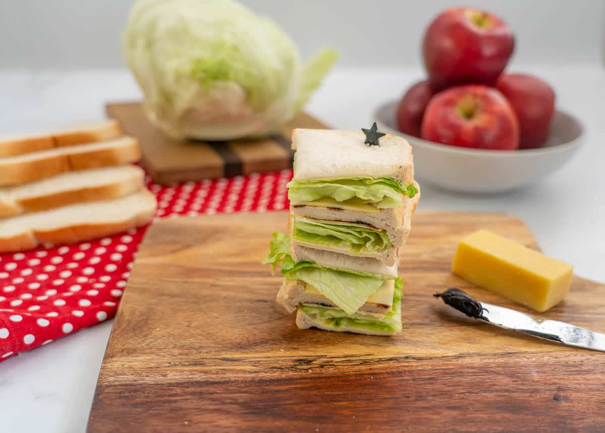 A stack of 4 small sandwiches filled with lettuce, cheese and marmit