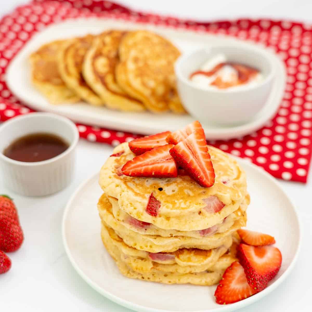 Stack of 5 thick strawberry pancakes with on a white plate with more pancakes in the background