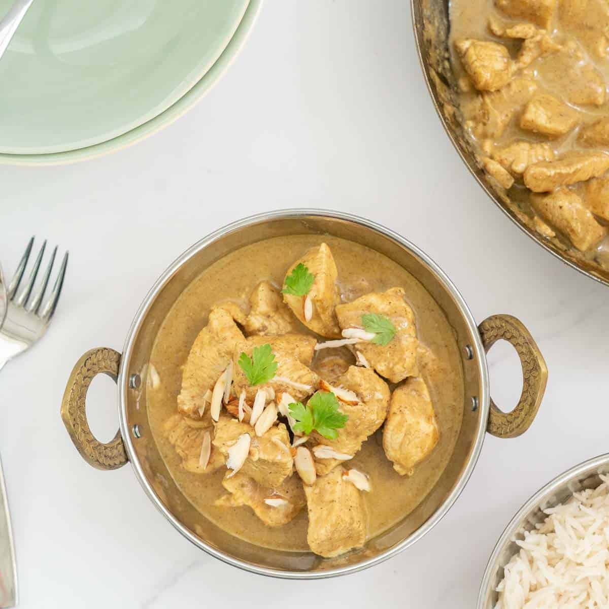 A copper bowl of chicken korma garnished with coriander leaves