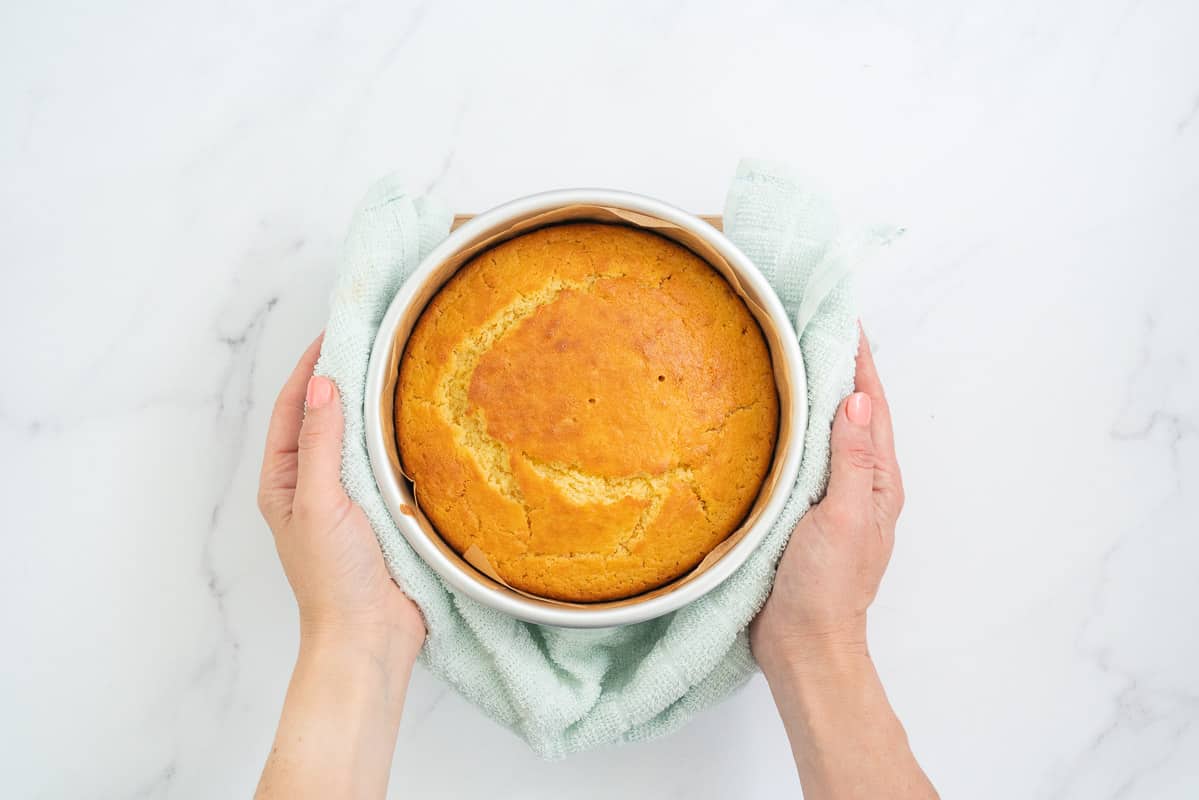 Cake in a cake tin, held by female hands with a tea towel