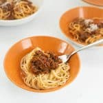 Spaghetti with bolognese sauce in an orange ceramic bowl.