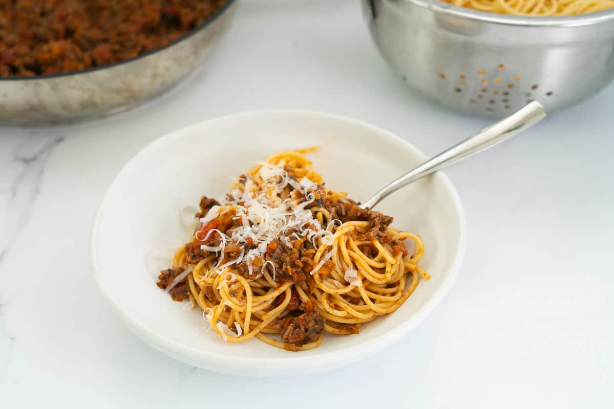 spaghetti bolognese in a white bowl with shaved parmesan cheese on top