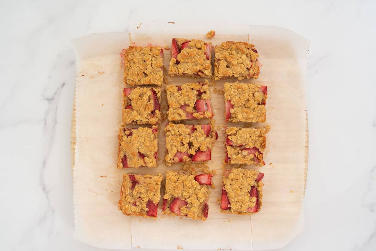 12 square pieces of strawberry crumble bar on a wooden chopping board