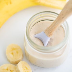 small glass jar filled with pudding, slices of banana next to the jar.
