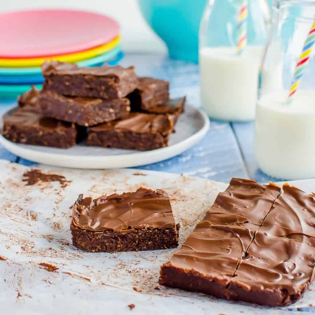 Pieces of chocolate slice on a blue table top with bottles of milk and straws.