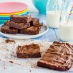 Pieces of chocolate slice on a blue table top with bottles of milk and straws.
