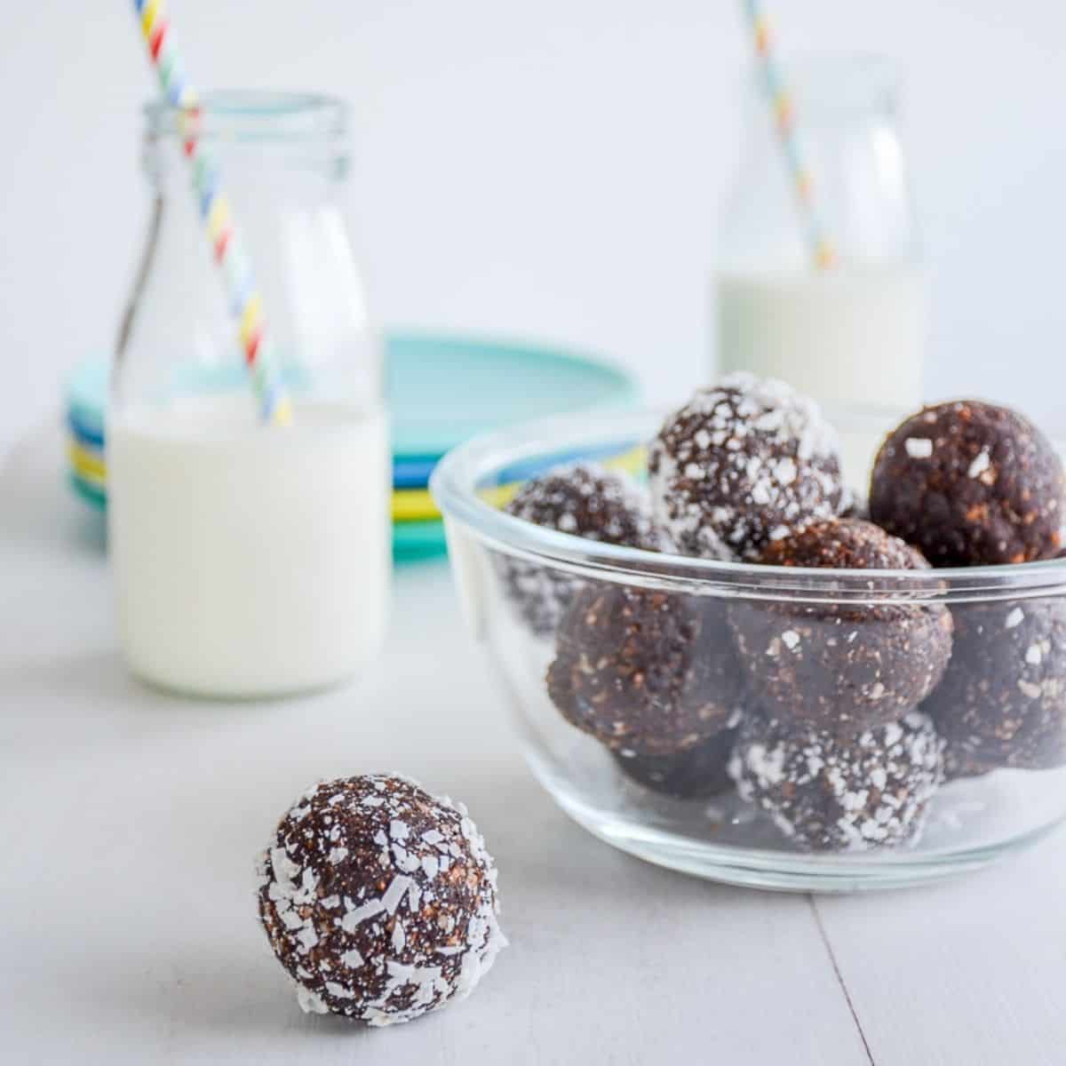 Chocolate bliss balls in a glass bowl with a bottle of milk.
