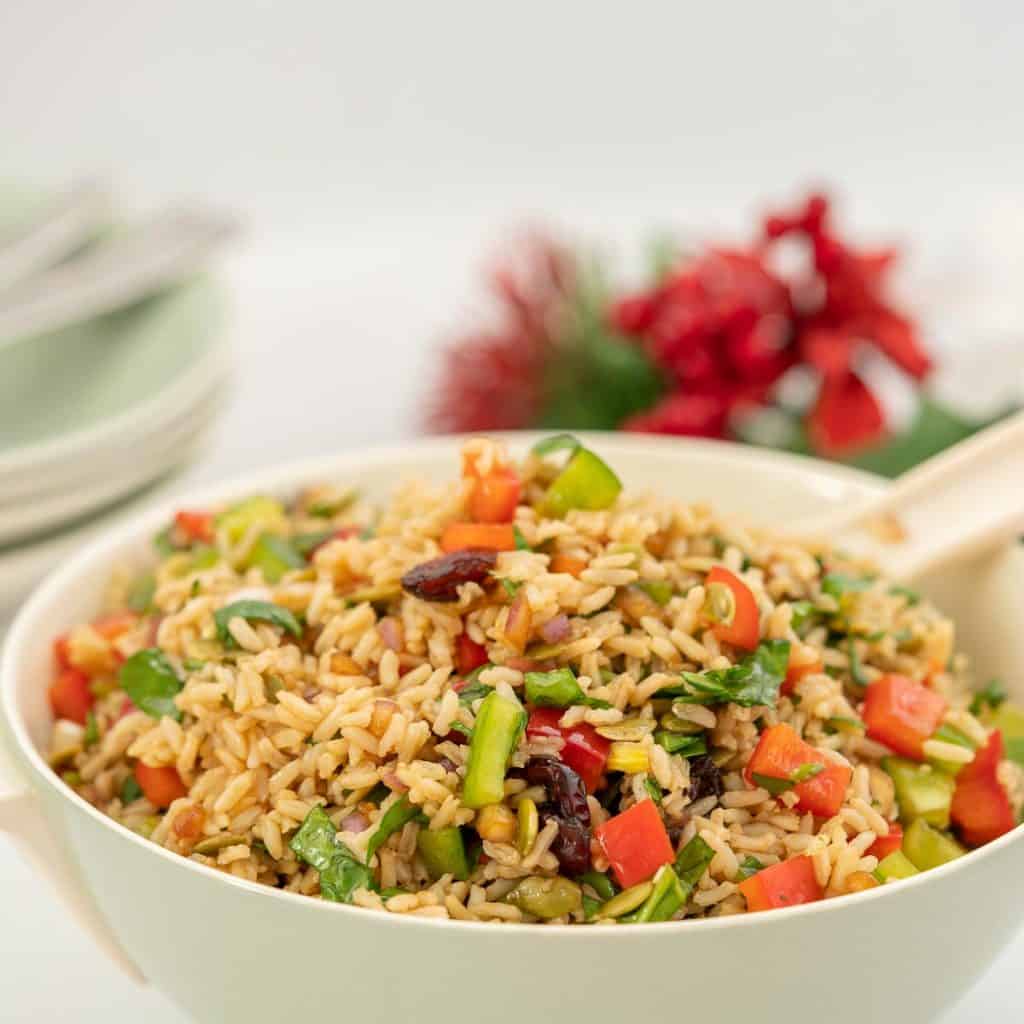 Large bowl of brown rice salad with red and green diced capsicum .