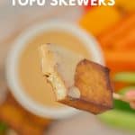 A hand holding a piece of baked tofu on a skewer, a mouthful has been eaten, revealing the creamy white centre of the tofu with text overlay for pinterest