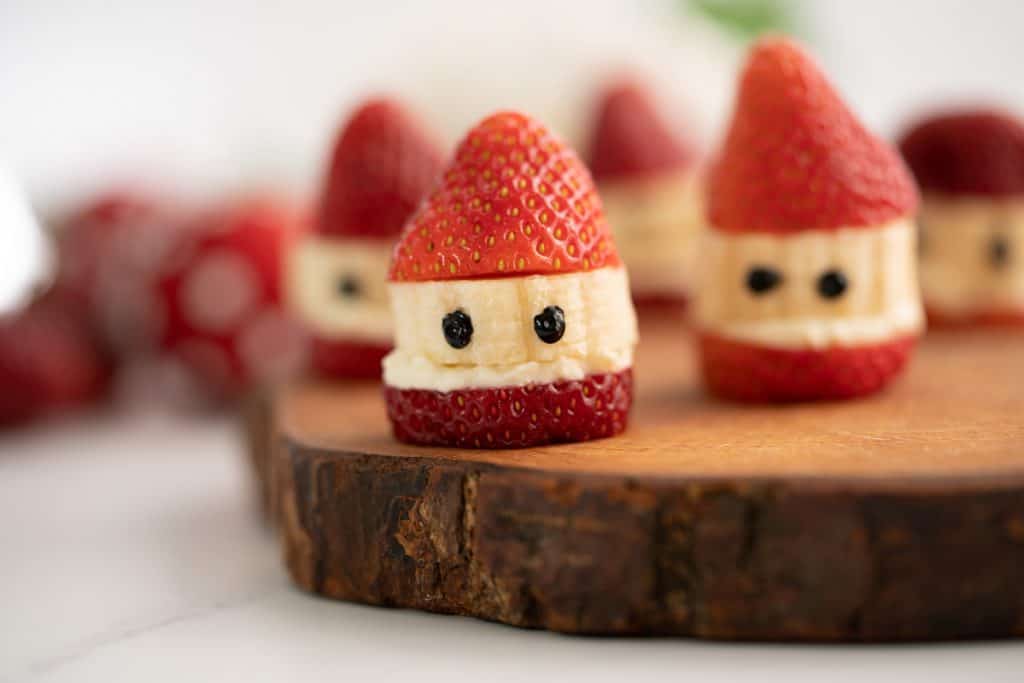Strawberry Santas sitting on a wooden board.