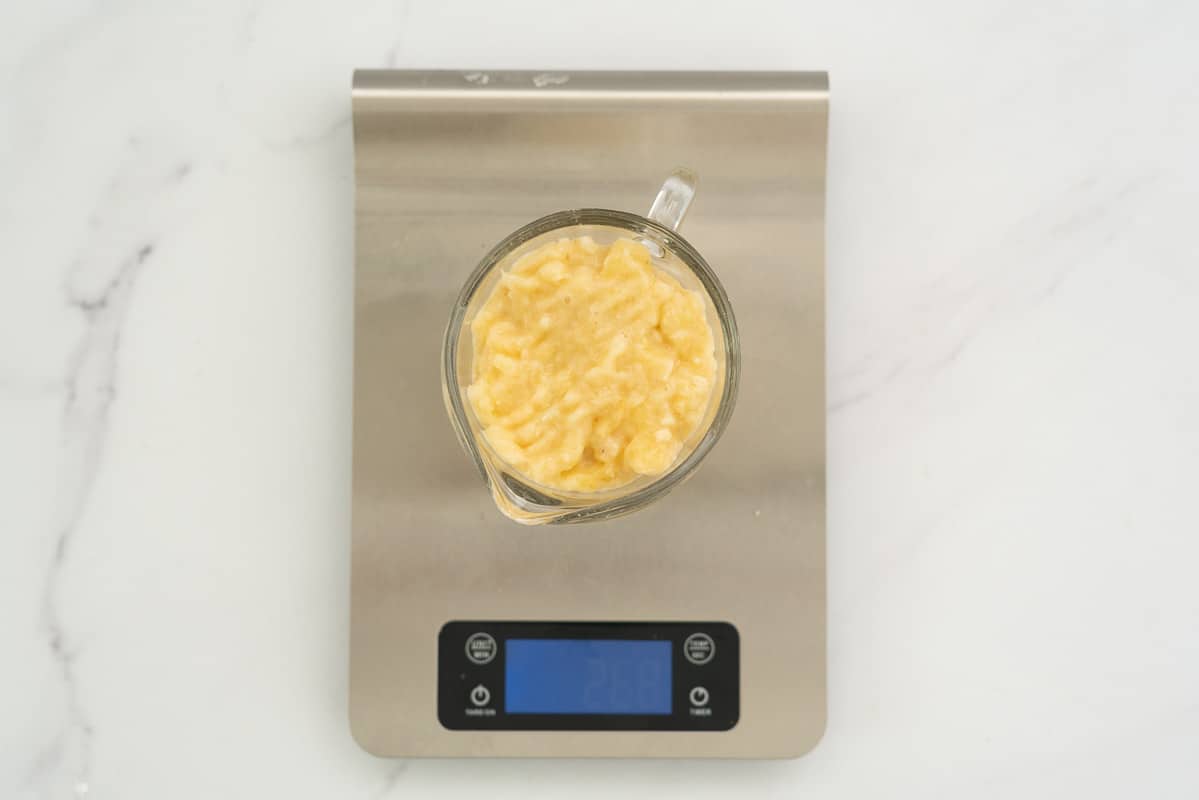 measuring cup of mashed banana on a digital kitchen scale weighing 268g