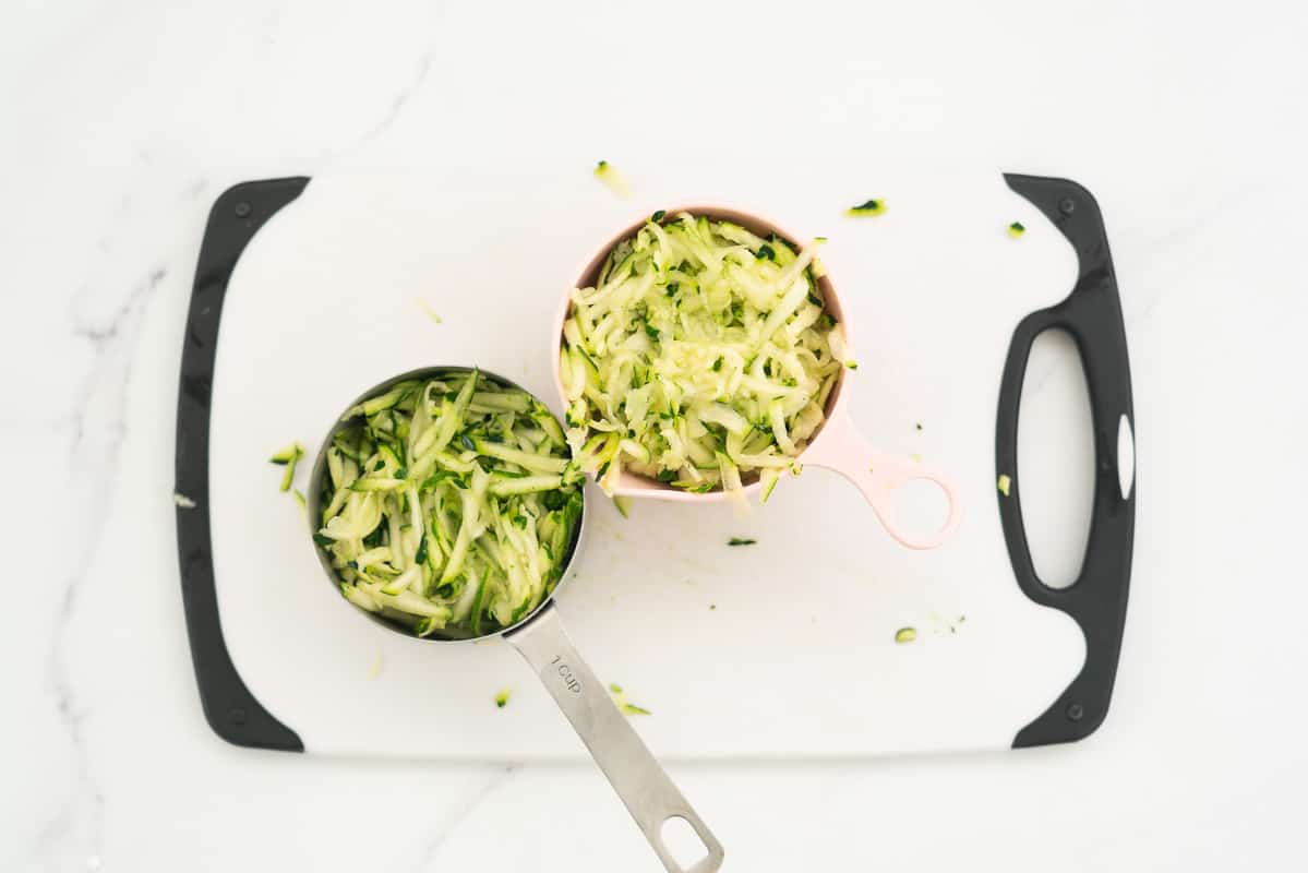 2 measuring cups of grated zucchini sitting on a white chopping board