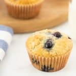 A blueberry muffin sitting next to a glass of milk and a blue and white cloth.