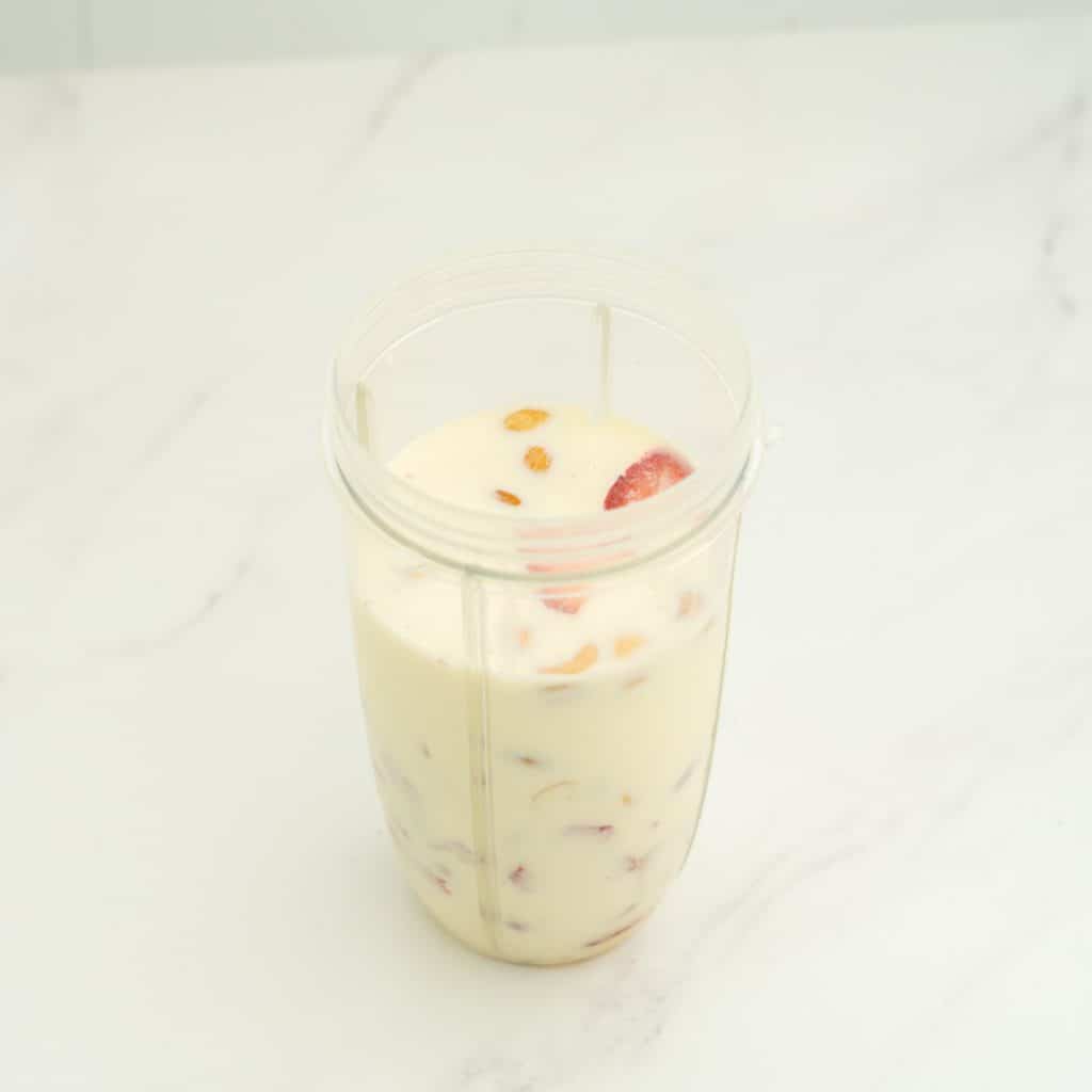Ingredients in a nutribullet blender cup, milk, strawberries, cashews visible.