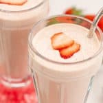 A close up of Two strawberry milkshakes in tall glasses topped with strawberry slice with red napkins.