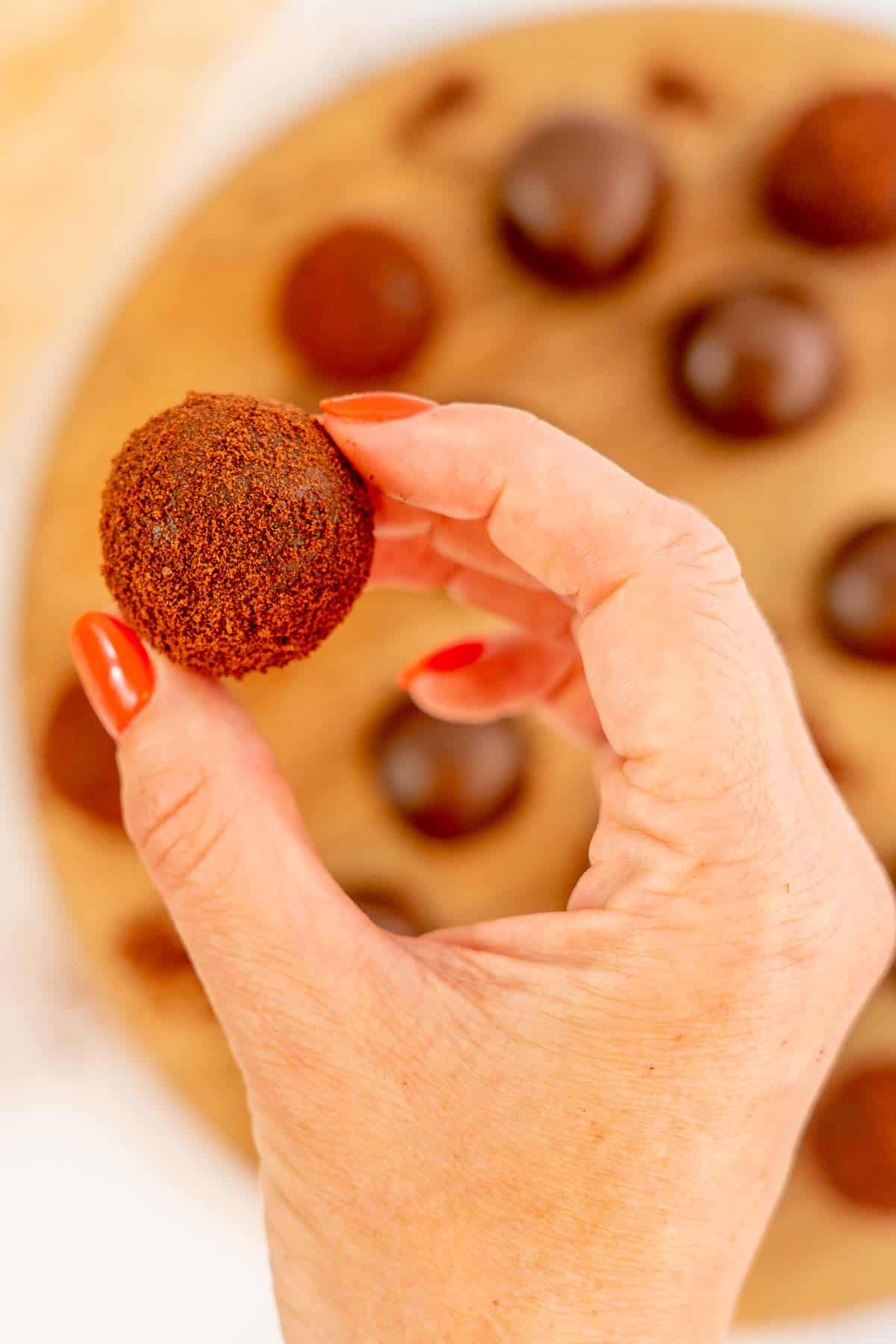 A woman's hand holding a milo ball above a wooden serving board of milo balls.