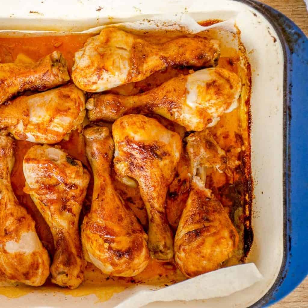 Baked paprika drumsticks in a baking paper lined blue oven dish.