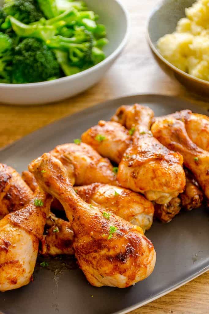 paprika-chicken-drumsticks on a platter with a large bowl of green vegetables and potato mash