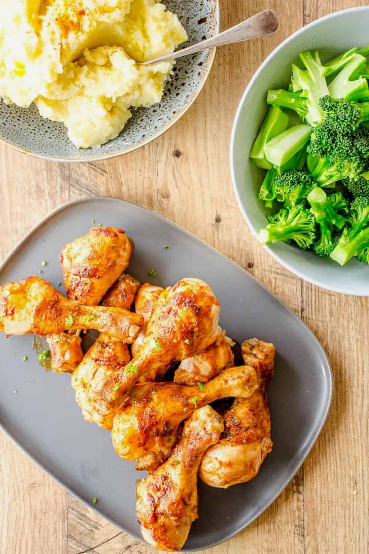 Family dinner meal with a platter of  chicken drumsticks, bowl of broccoli and a bowl of mash.