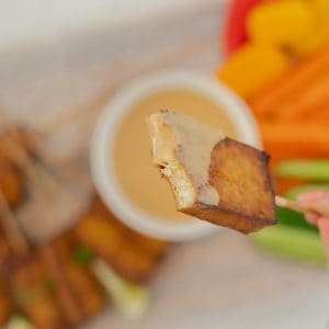 A hand holding a piece of baked tofu on a skewer, a mouthful has been eaten, revealing the creamy white centre of the tofu.