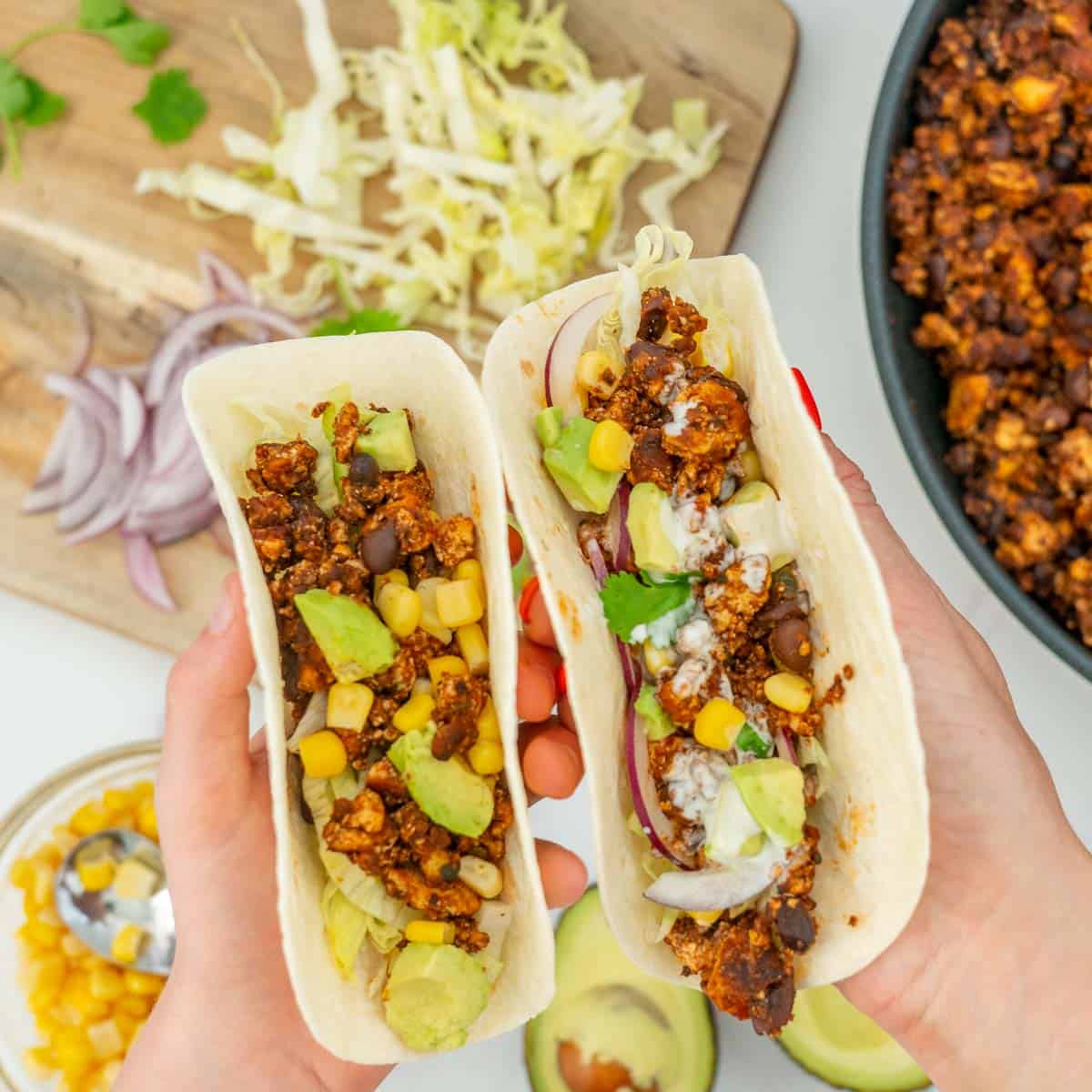 A woman's hand and a child's hand holding soft tacos filled with Mexican tofu crumbles