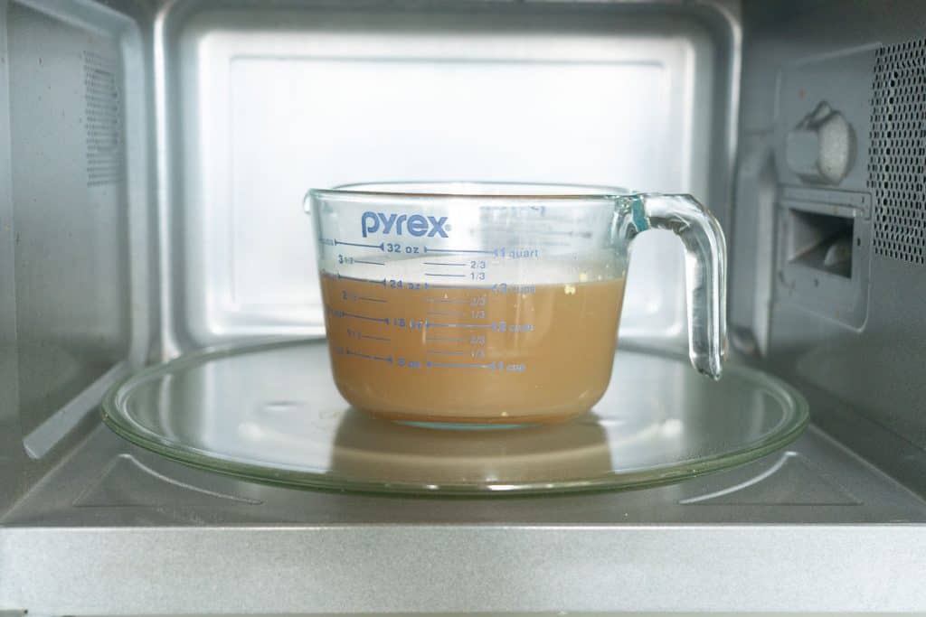 A glass measuring jug full of stock sitting in a microwave.