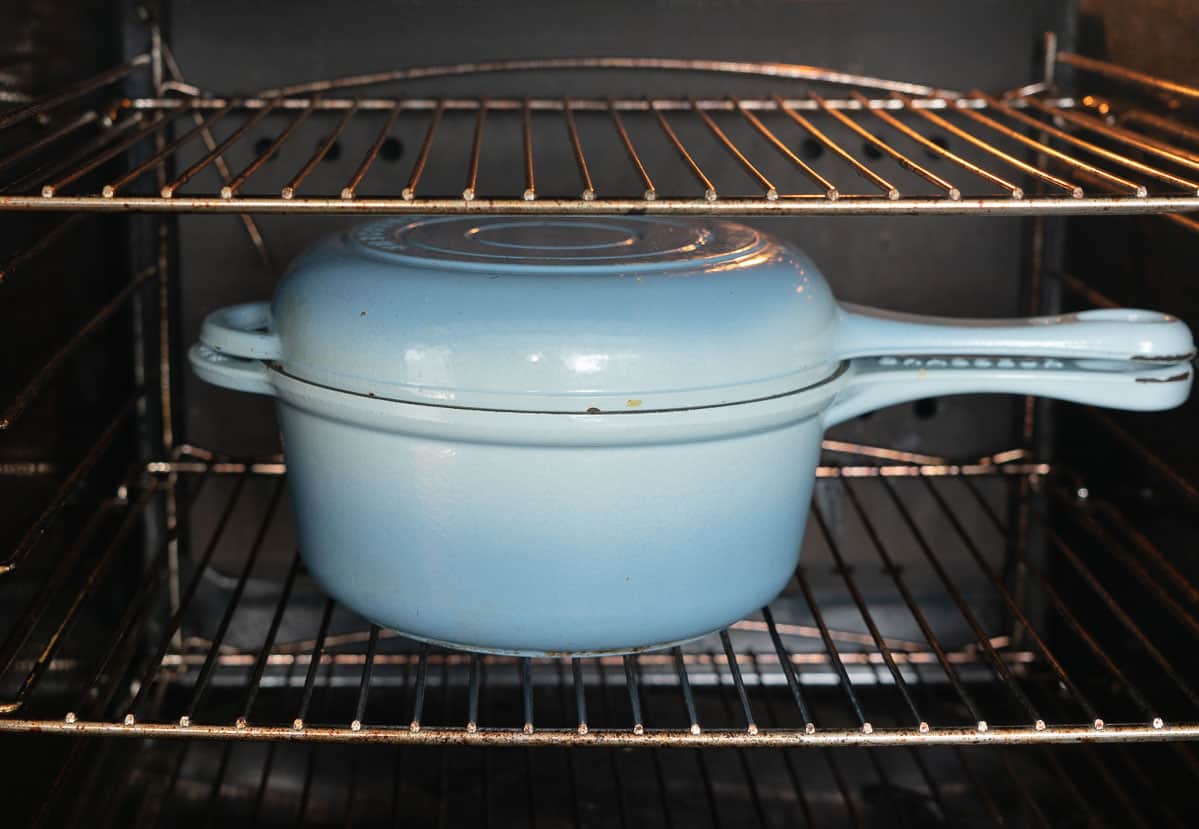 Large blue ceramic oven dish with lid on inside an oven.
