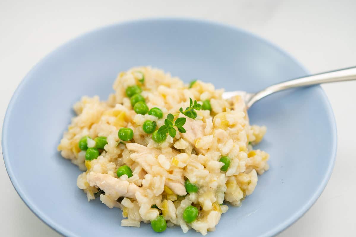 A blue bowl filled with risotto, leeks, chicken and peas visible