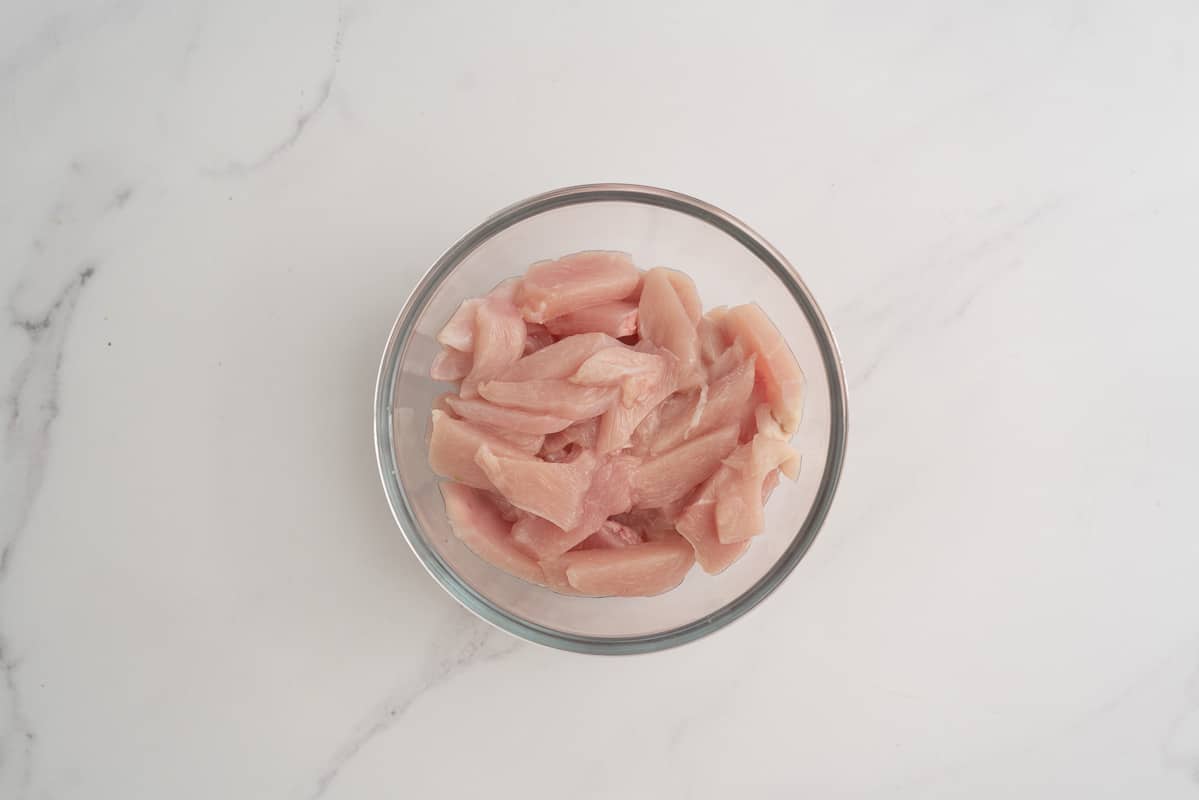 A glass bowl of finely sliced chicken breast.