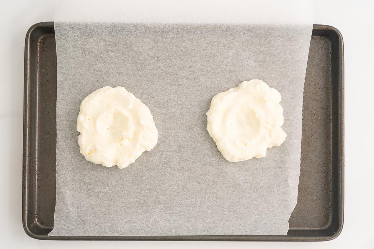 Beaten egg whites shaped like  2 clouds with a small indentation in the centre of each one.