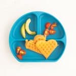 a blue silicone divided plate with 2 heart shaped egg waffles, sliced tomatoes and avocado.