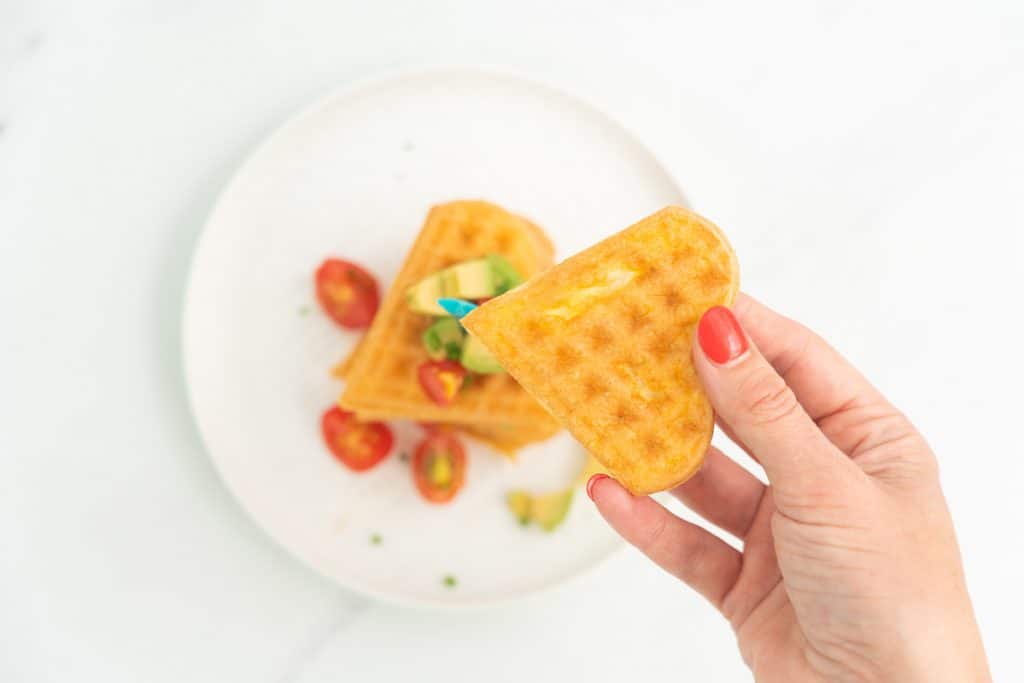 Woman's hand holding a heart shaped segment of an egg waffle.