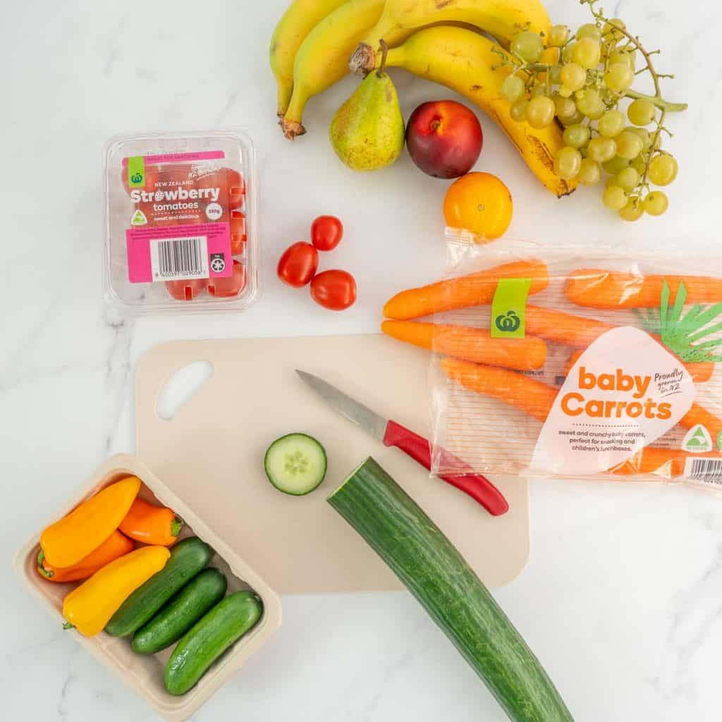 Fresh produce for lunchboxes, fruits and vegetables on a bench with a knife and chopping board