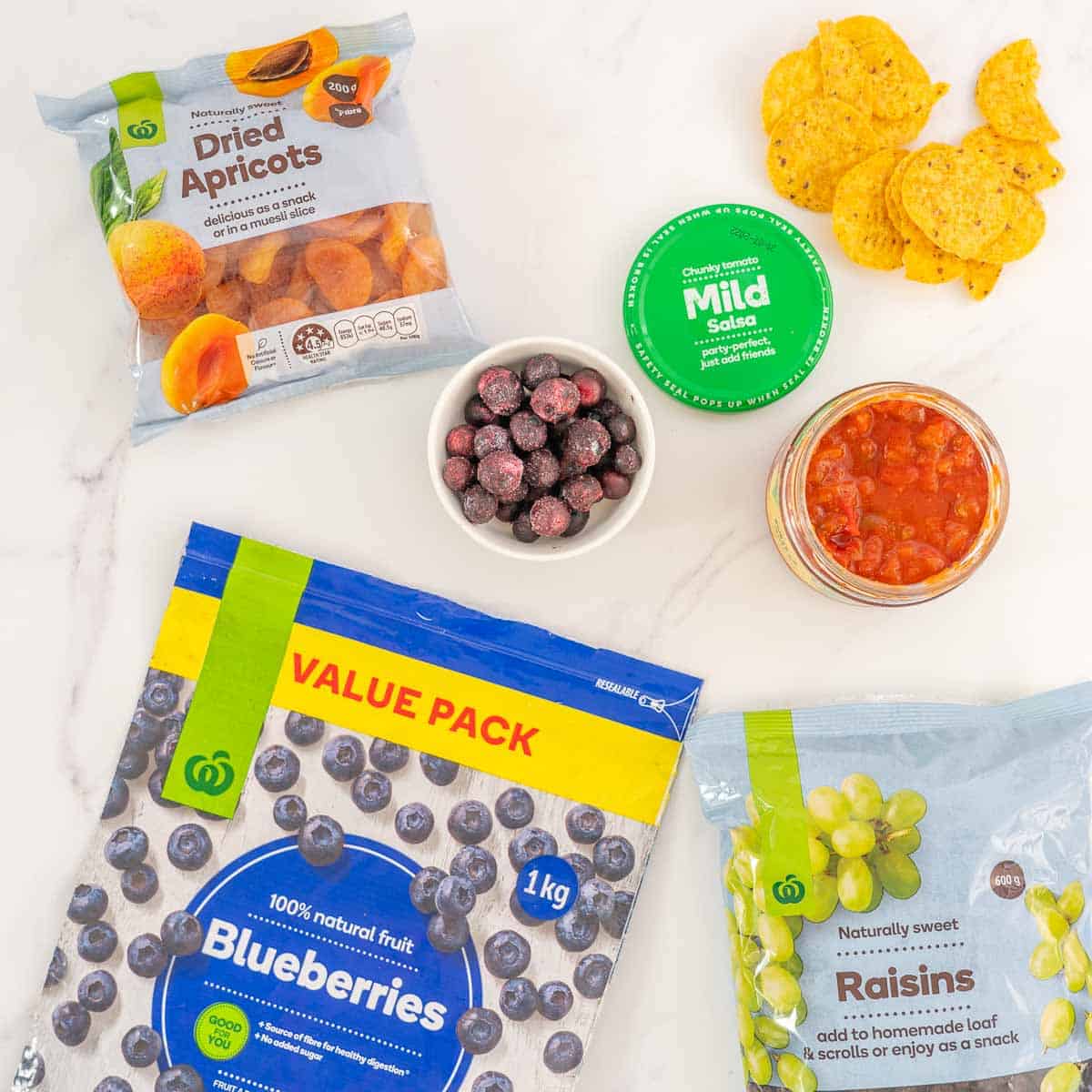 Frozen blueberries, dried apricots, raisins and a jar of salsa laid out on a bench top. 