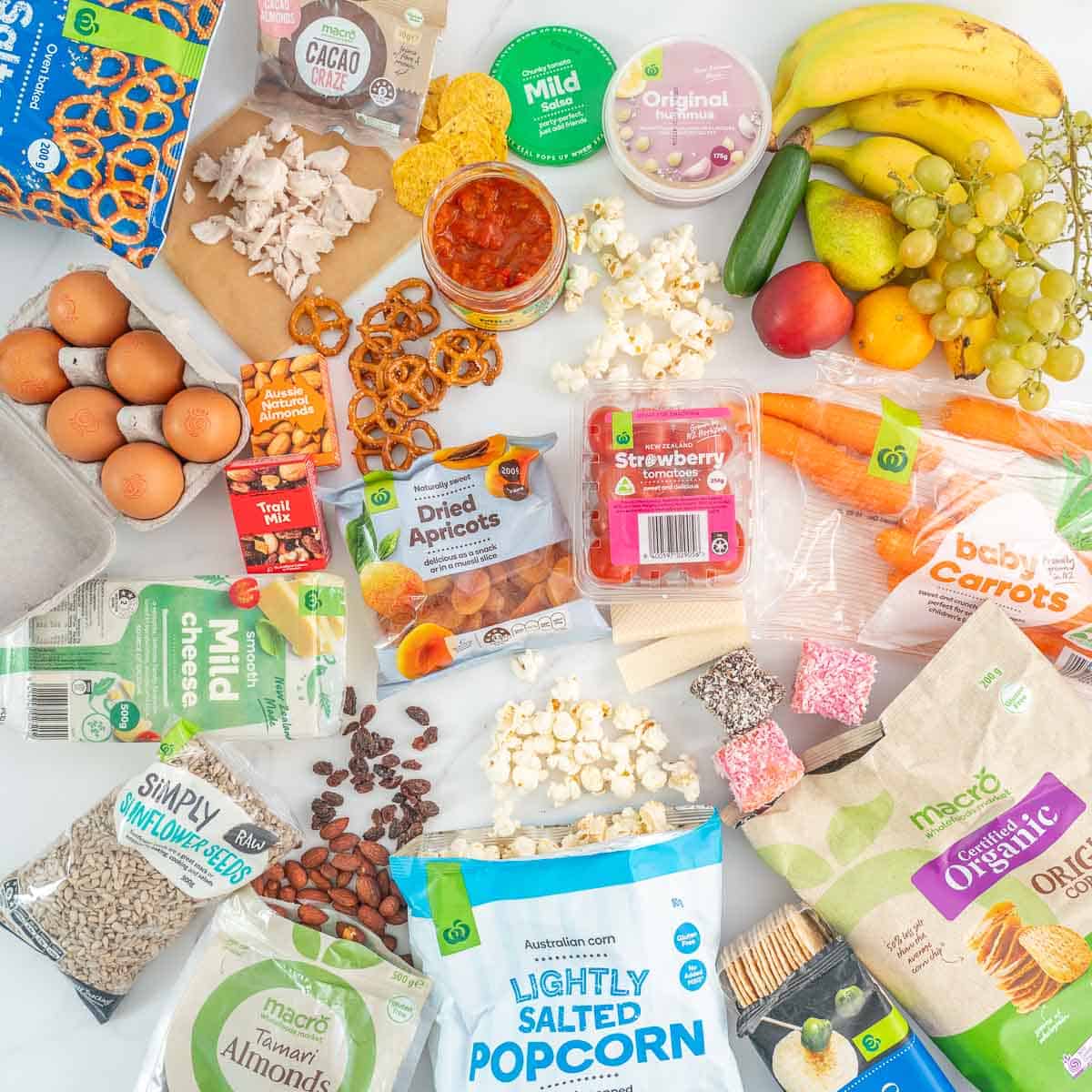 A collection of lunch box snacks you can grab at a supermarket laid out on a bench.