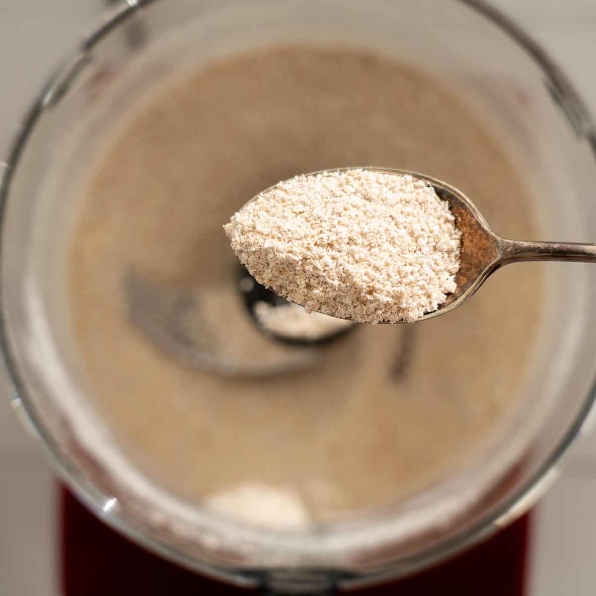 A spoonful of oat flour above a food processor.