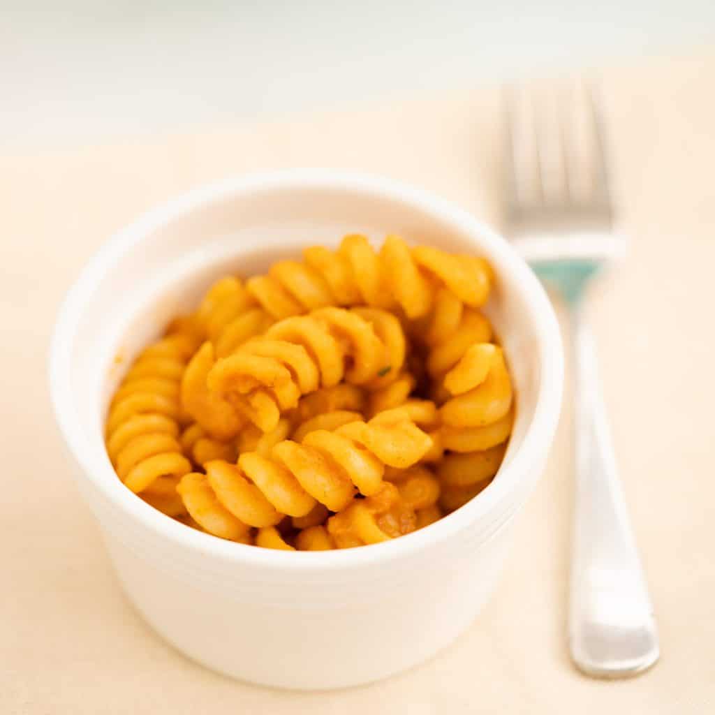 Sauce covered pasta spirals in a small white ceramic bowl.