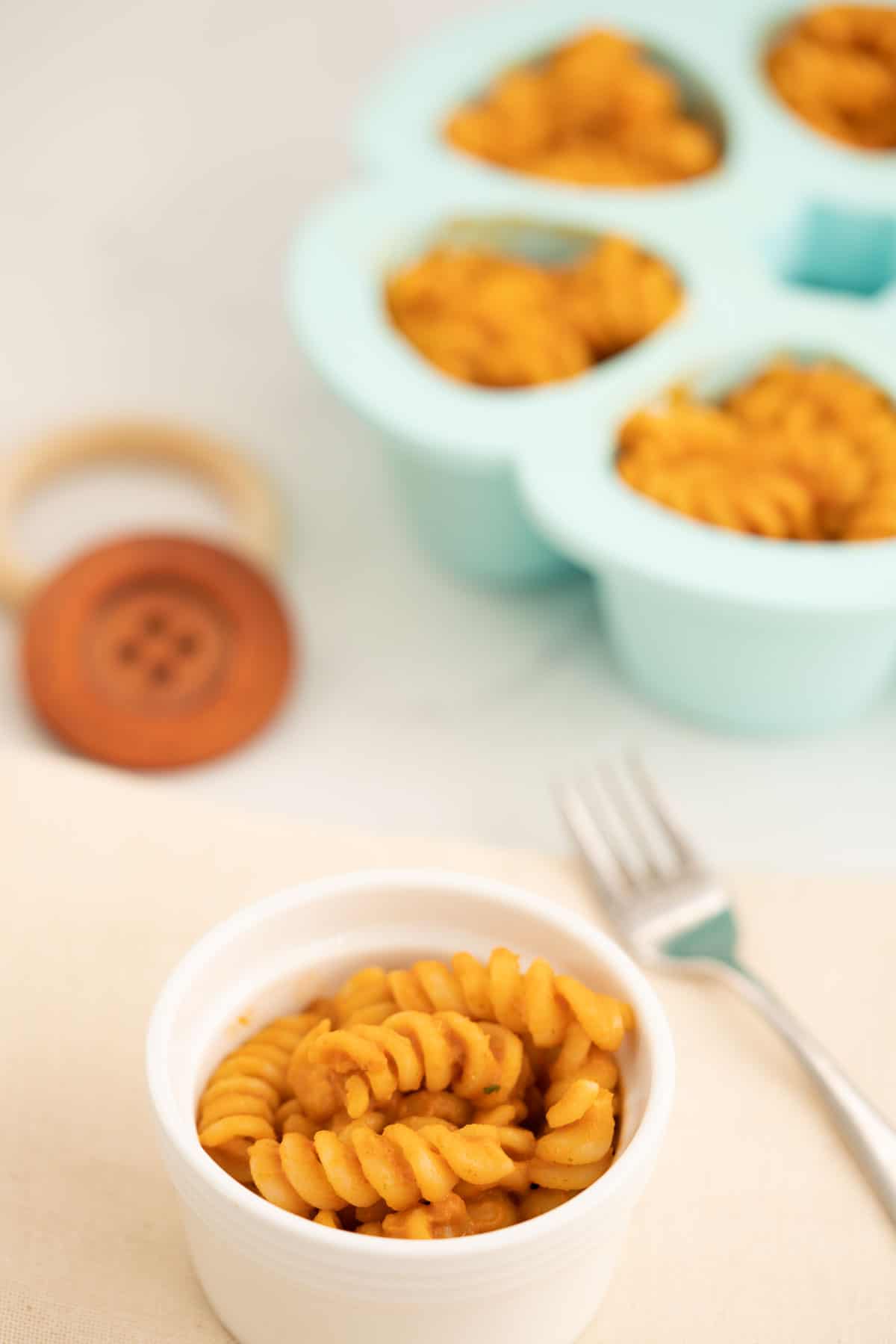 A bowl of baby pasta with a blue silicone baby portion freezing container in the background.