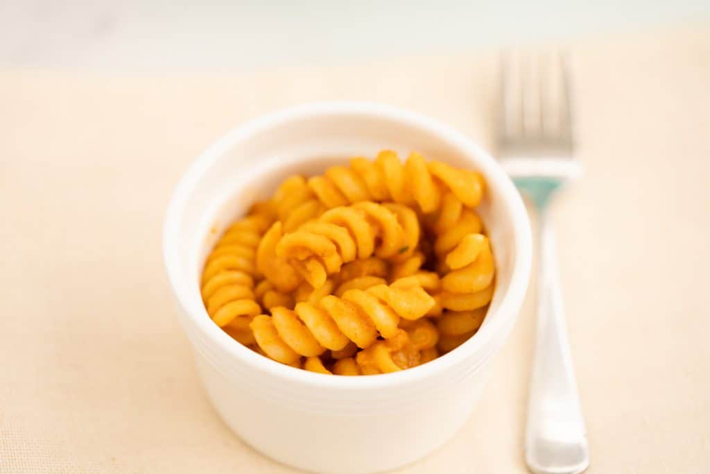 Sauce covered pasta spirals in a small white ceramic bowl.