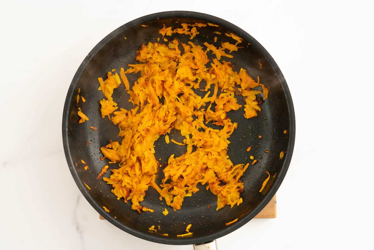 Golden sautéed grated carrot and pumpkin in a fry pan.