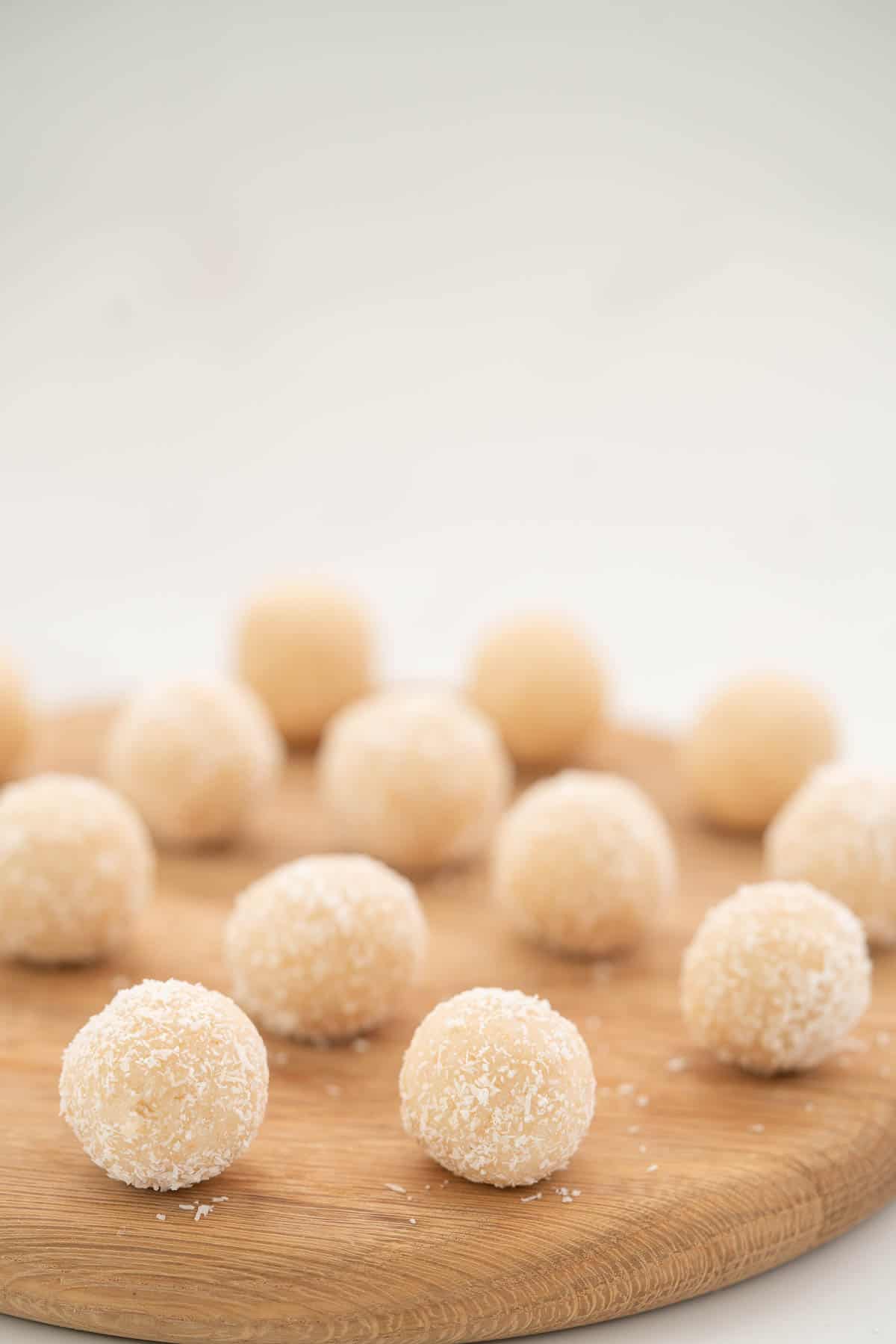 White coconut balls served on a round woodden board.