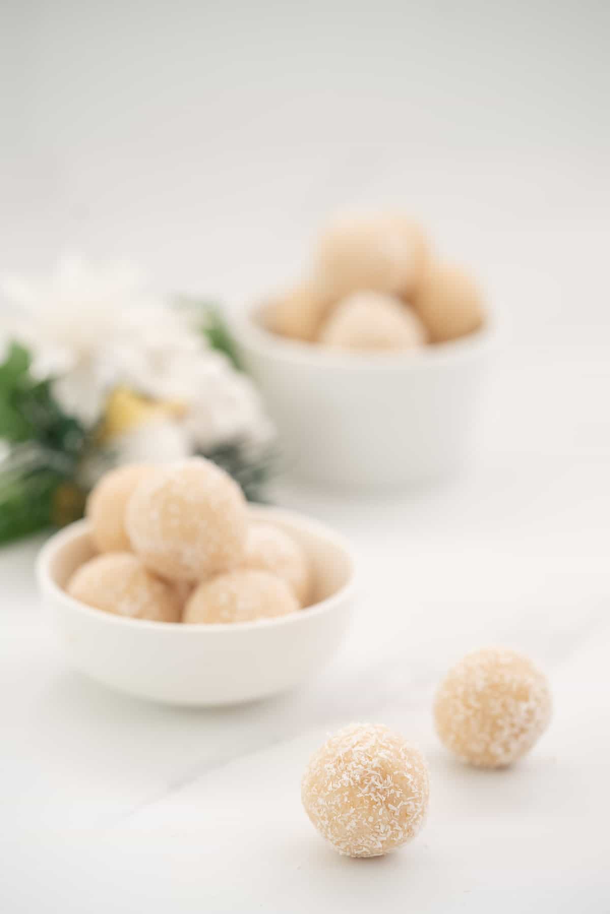 Coconut balls on a white marble bench top with christmas decorations in the background.