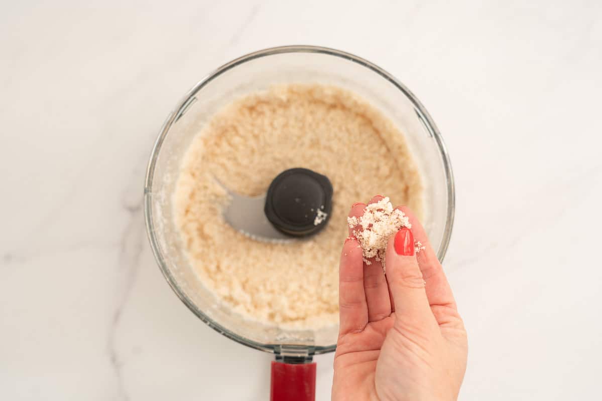 Women's hand holding finely ground rice bubbles and coconut, looks a little bit like fine soft sand.